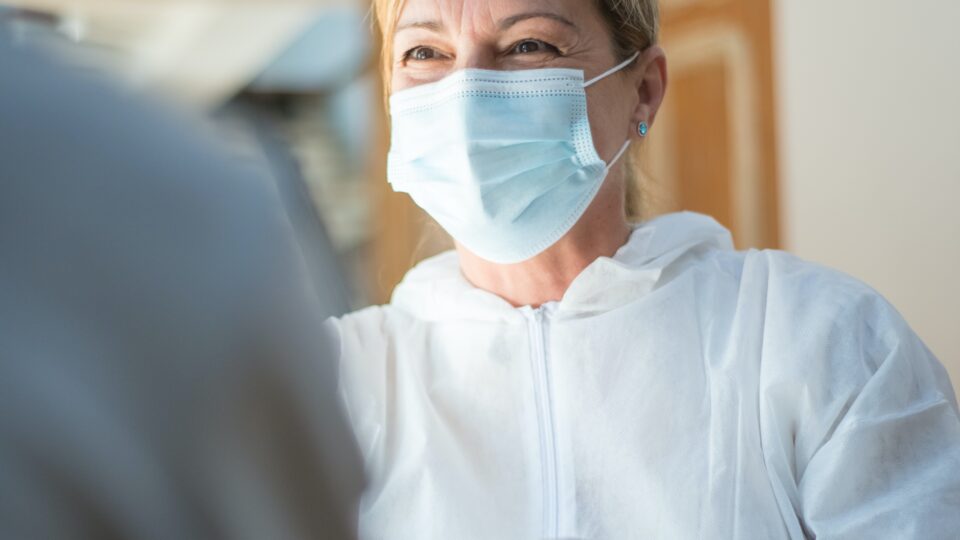 Frau mit Maske sitzt Patienten gegenüber