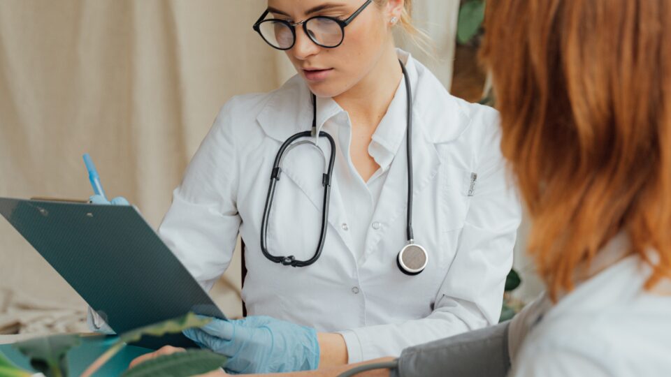 Ärztin analysiert Krankenakte. Blutdruckmesser ist an einer anderen Frau angeschlossen.