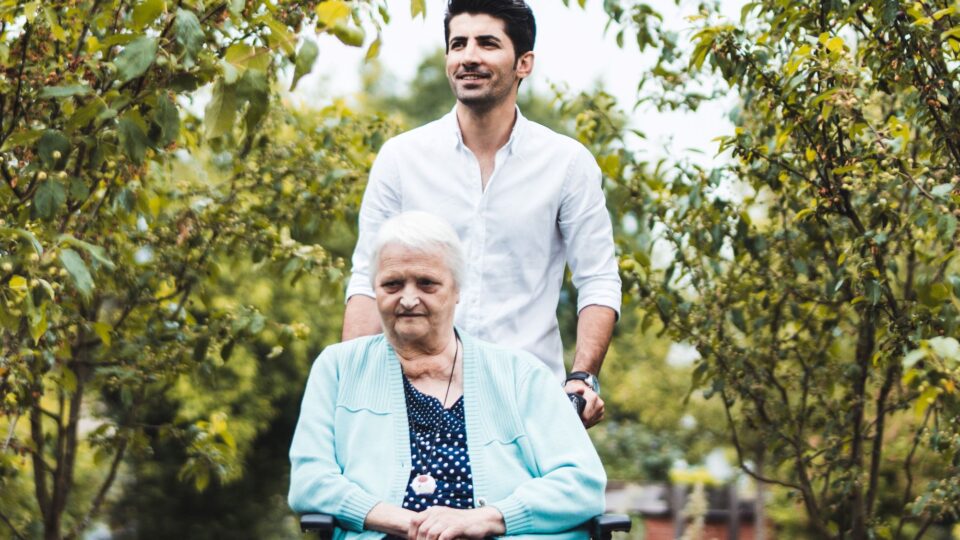 Junger Mann schiebt Rollstuhl mit älterer Frau